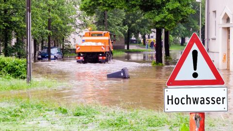 Überschwemmte Straße und Schild mit "Hochwasser" als Aufschrift