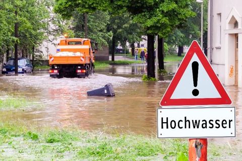 Überschwemmte Straße und Schild mit "Hochwasser" als Aufschrift